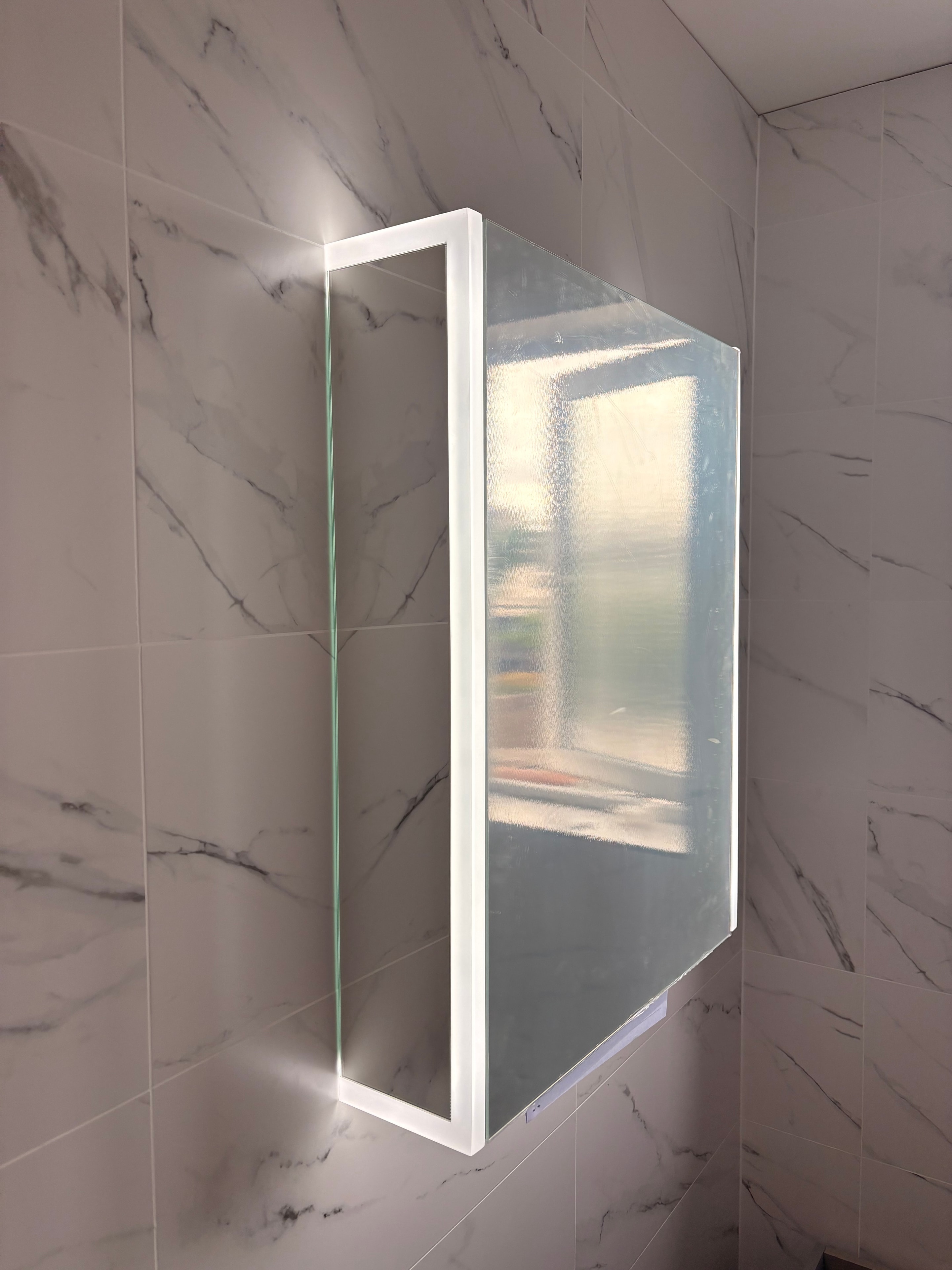 Close-up of smart bathroom mirror showing integrated Bluetooth speaker grille, LED lighting strip and toothbrush holder detail — Staines bathroom renovation
